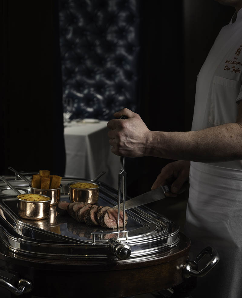 Chef carving roasted meat on silver service trolley with copper side dishes